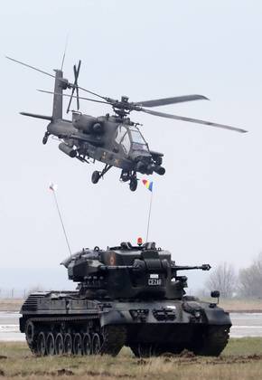 Nesta foto, militares em um helicóptero Apache, dos EUA, se aproximam de um tanque militar em terra