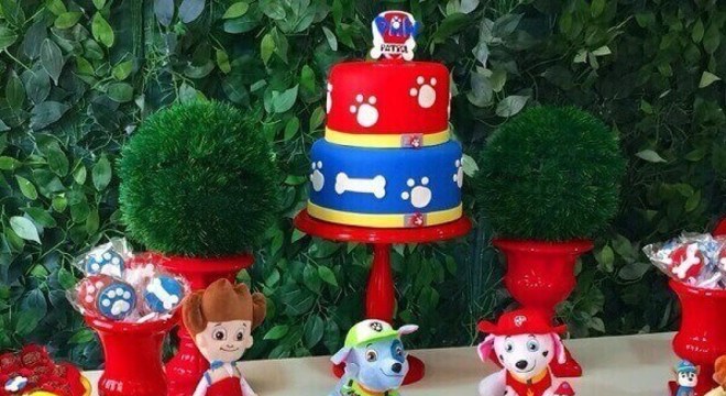 Elementos decorativos na cor vermelha se destacam na mesa do bolo