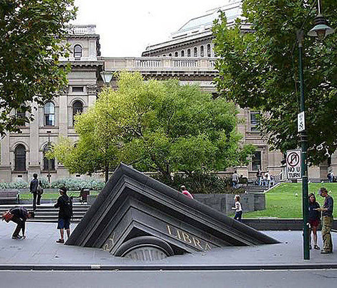 Essa escultura fica em frente à Biblioteca do Estado de Melbourne, na Austrália, e retrata uma Library, ou seja, biblioteca em inglês, afundando com o peso dos livros na calçada. 