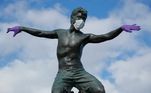 em uma praia da Califórnia, nos Estados Unidos, uma estátua de surfista usa lucas e máscaras de proteção