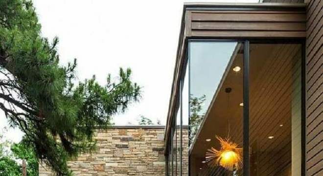 fachada casa em l moderna com paredes de vidro e revestimento de pedra