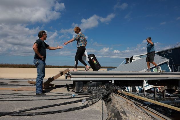Homem ajuda mulher a atravessar uma ponte provisória após o furacão ter destruído a estrada que havia no local, em Pine Island