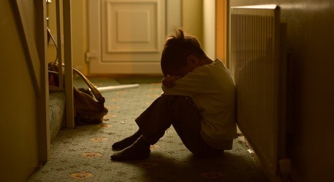 Foto ilustrativa sobre abuso infantil - menino chora sentado no corredor de casa