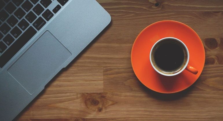 Fotografia de um café preto numa mesa com notebook para ilustração do item