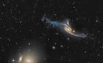 Com mais de 500 mil anos-luz de diâmetro, a NGC 6872, no canto superior direito da imagem, é uma galáxia espiral enorme, com pelo menos cinco vezes o tamanho da nossa Via Láctea