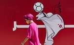 Uma mulher passa por uma cerca de um canteiro de obras mostrando uma ilustração do mascote da Copa do Mundo 'La'eeb' em West Bay, na capital do Catar, Doha, em 13 de outubro de 2022