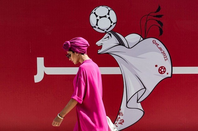 Uma mulher passa por uma cerca de um canteiro de obras mostrando uma ilustração do mascote da Copa do Mundo 