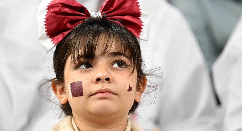 Garotinha pinta o rosto com a bandeira do Catar na arquibancada do estádio Al Bayt