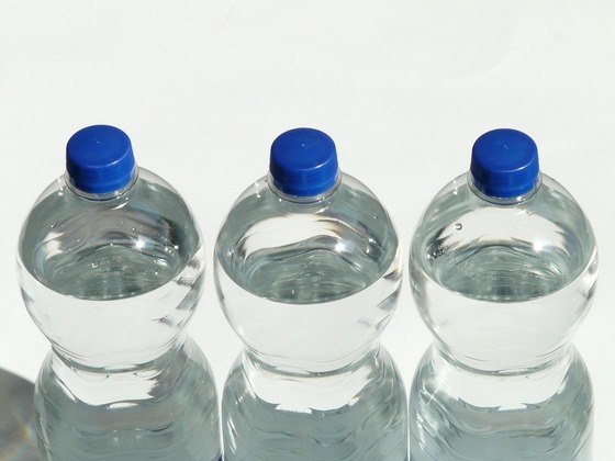 três garrafas plásticas com tampas azuis cheias de água
