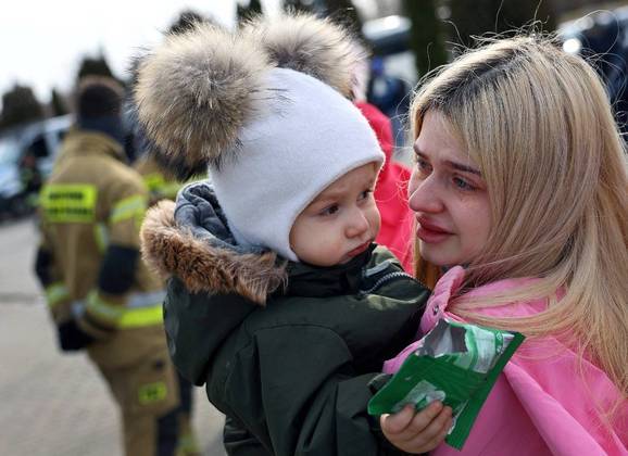 Uma mulher chora enquanto segura seu filho depois de fugir da Ucrânia por causa da invasão russa quando eles chegaram com um ônibus na vila de Moszczany perto do posto de fronteira em Korczowa, Polônia