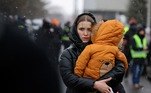 Uma mulher carrega uma criança depois de fugir da invasão da Ucrânia pela Rússia, na fronteira em Siret, Romênia