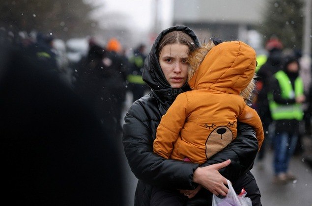Uma mulher carrega uma criança depois de fugir da invasão da Ucrânia pela Rússia, na fronteira em Siret, Romênia