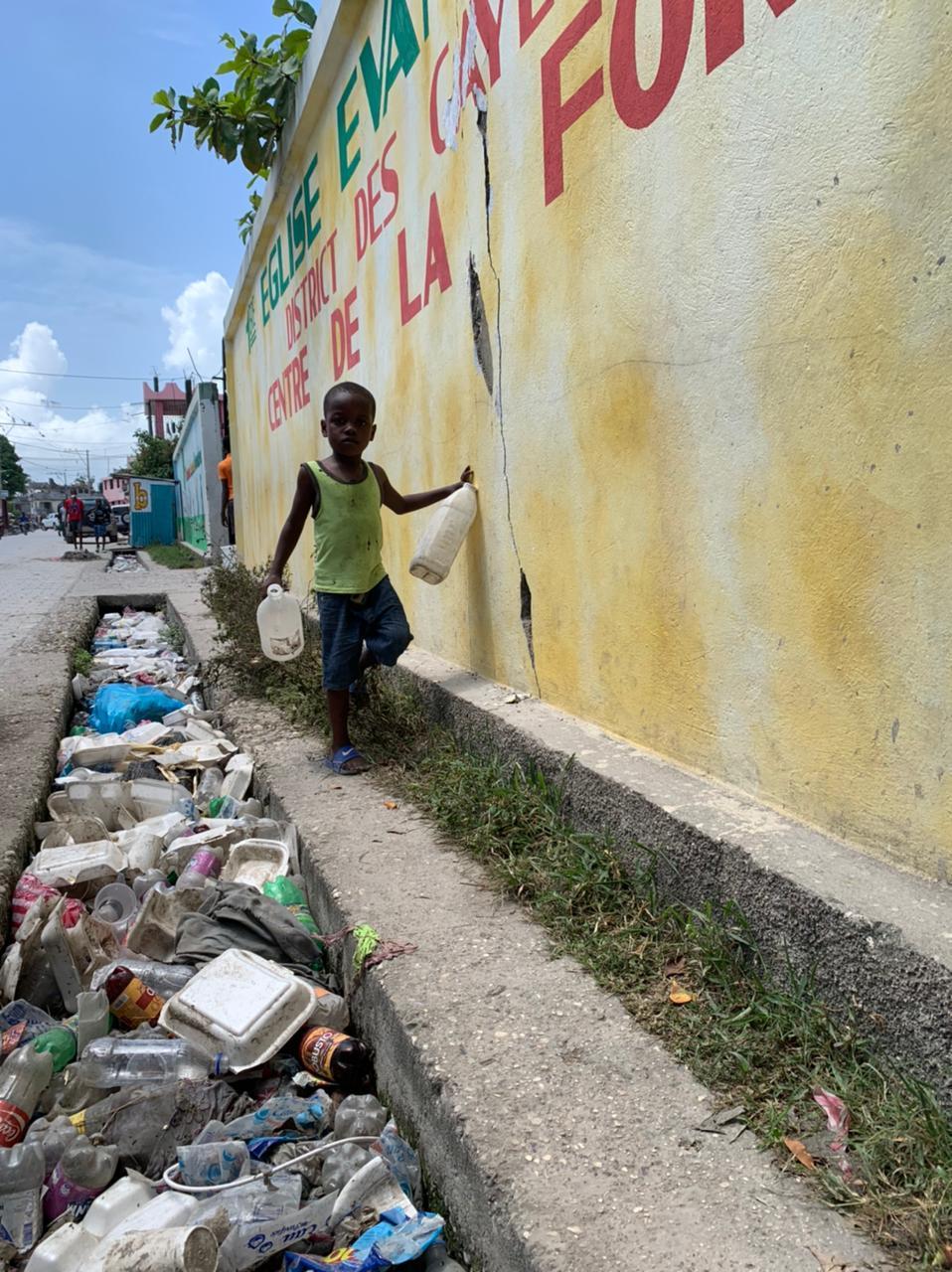 Menino caminha ao lado de fosso sujo na beira do estádio de Les Cayes (RecordTV)