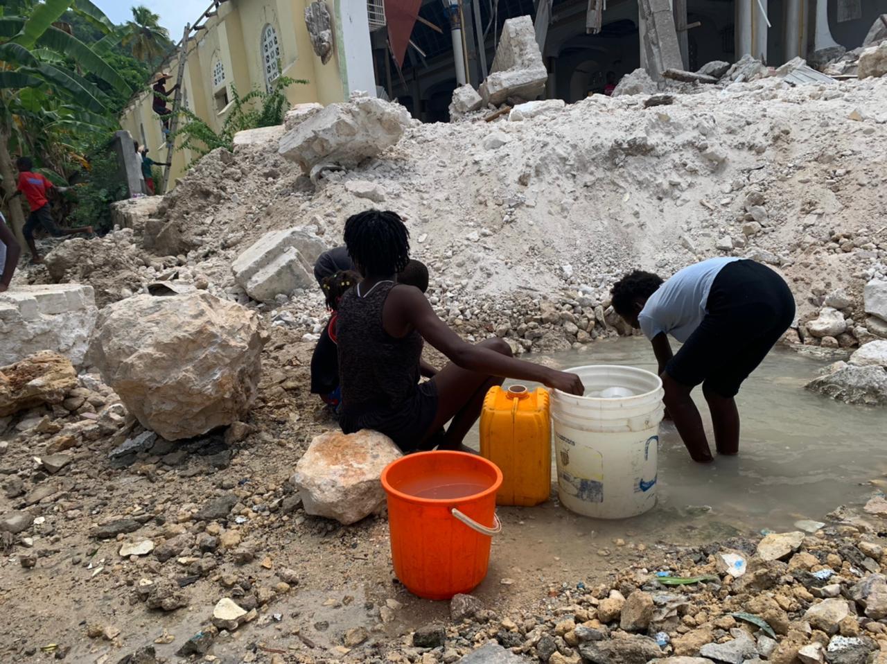 Crianças pegam água para consumo em meio aos escombros de uma igreja desabada em Corail (RecordTV)