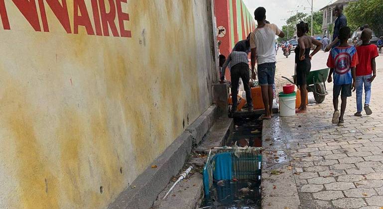 Bica de água em muro do estádio, ao lado de fosso sujo, utilizada para beber e para lavar panelas em Les Cayes