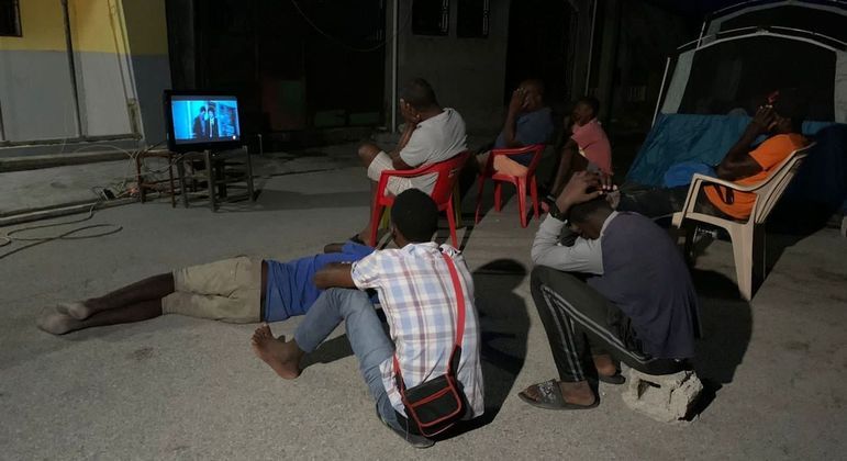 Homens se juntam para assistir novela coreana em Les Cayes, enquanto mulheres dormem em tendas