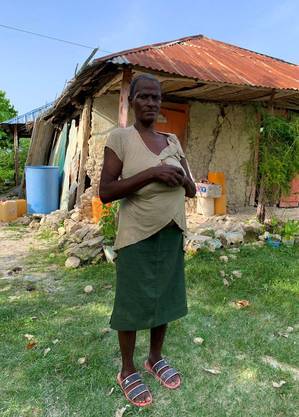 Cima Gladys, 57, em frente à casa onde mora e onde continua dormindo