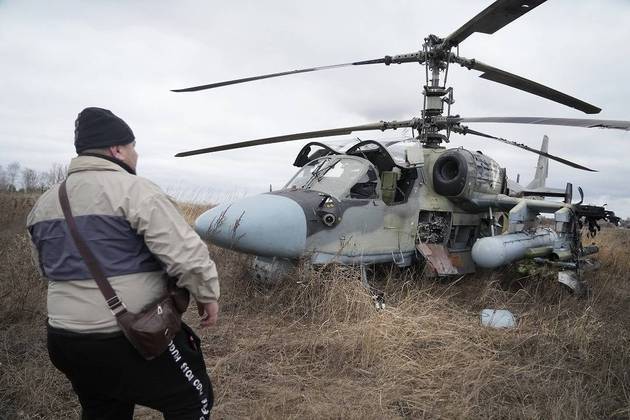 Homem observa um helicóptero russo Ka- 52 após um pouso forçado num campo nos arredores de Kiev, na Ucrânia. Grandes explosões foram ouvidas antes do amanhecer em Kiev, Kharkiv e Odesa, enquanto os líderes mundiais denunciavam o início de uma invasão russa que poderia causar baixas em massa e derrubar o governo democraticamente eleito da Ucrânia