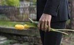 Homem de terno segura tulipa amarela em um cemitério. Freepik