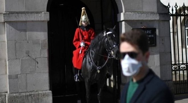 Um homem usando uma máscara protetora passa por um membro da cavalaria britânica em Whitehall