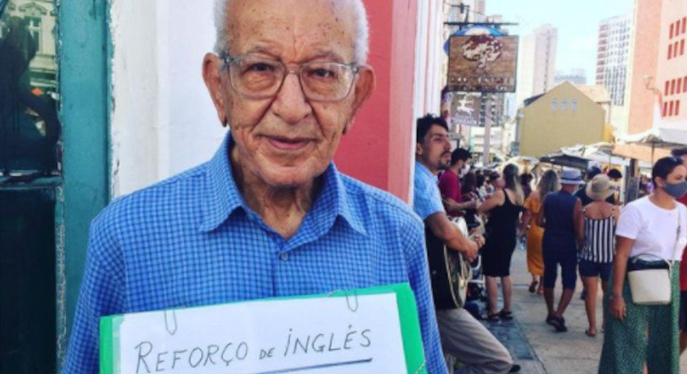 Sr. Henrique caminha pelas ruas de Curitiba carregando sua plaquinha: ele dá aula grátis de inglês