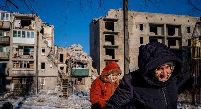 Idosos de Chasiv Yar, na Ucrânia, passam por um prédio residencial destruído