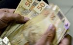 Imagem da mão de uma pessoa contando notas de R$ 50. 