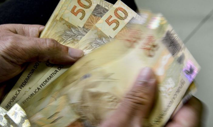 Imagem da mão de uma pessoa contando notas de R$ 50. 