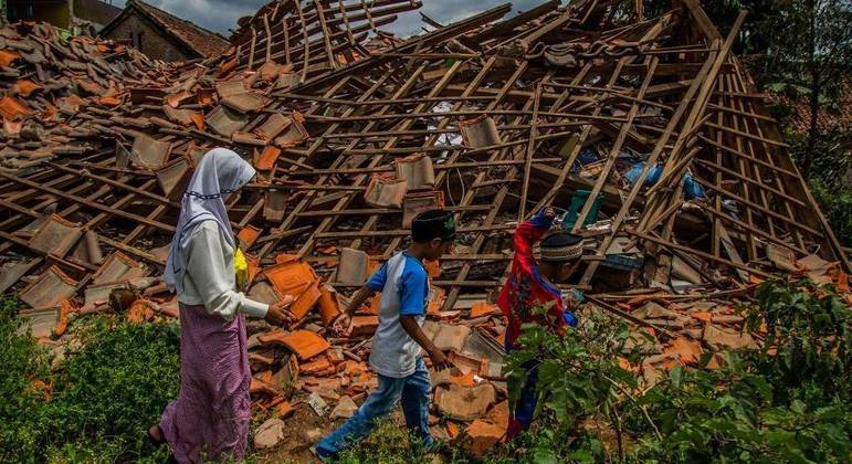 Crianças passam por uma casa que desabou após terremoto, em Java Ocidental