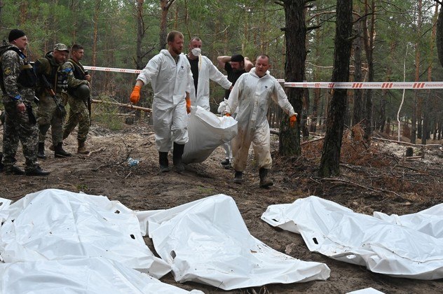 À direita da trilha, 100 metros dentro da floresta, segundo jornalistas da AFP, dois homens (de túnica branca) cavaram delicadamente a areia no fundo de uma sepultura, que tinha uma cruz e a inscrição: 'Exército ucraniano 17 pessoas. Izium, do necrotério'