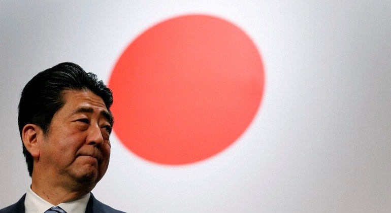 O ex-primeiro-ministro do Japão Shinzo Abe em frente à bandeira nacional do país