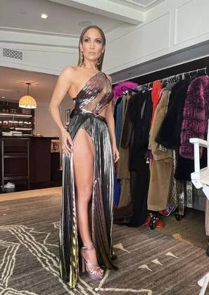 Em março, JLo usou um vestido metálico repleto de detalhes ousados: formato transversal, transparência e superfenda lateral. Sandália de salto prata e grandes brincos dourados arremataram o look