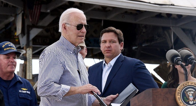 Presidente Joe Biden (à frente) e governador Ron DeSantis (atrás) em discurso na Flórida