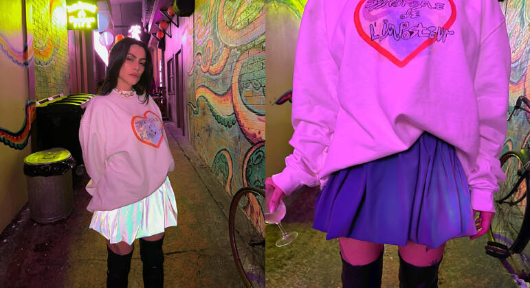Para aproveitar a noite da capital paulista, Cleo escolheu misturar conforto e estilo usando um moletom oversized com uma saia 'colegial' em tecido reflexivo (que está super em alta) e botas acima dos joelhos
