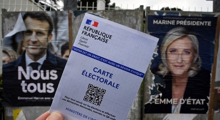 Cartão eleitoral é mostrado na frente de cartazes de Macron e Le Pen