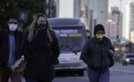 Duas mulheres usando casacos e máscaras de proteção caminham em frente a ônibus