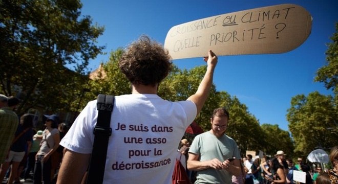 Manifestante protesta a favor do decrescimento na França em 2018, com cartaz em que se lê: ‘Crescimento ou clima, o que é prioridade?’