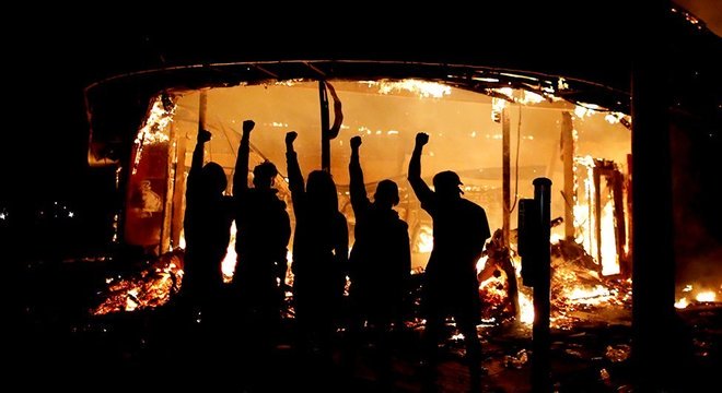 Manifestantes posam do lado de fora de loja de bebidas em chamas nos Estados Unidos