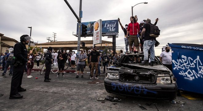 Manifestantes no topo de um carro da polícia queimado em Los Angeles, Califórnia