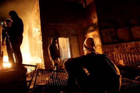 Manifestantes observam a entrada da delegacia incendiada em Minneapolis