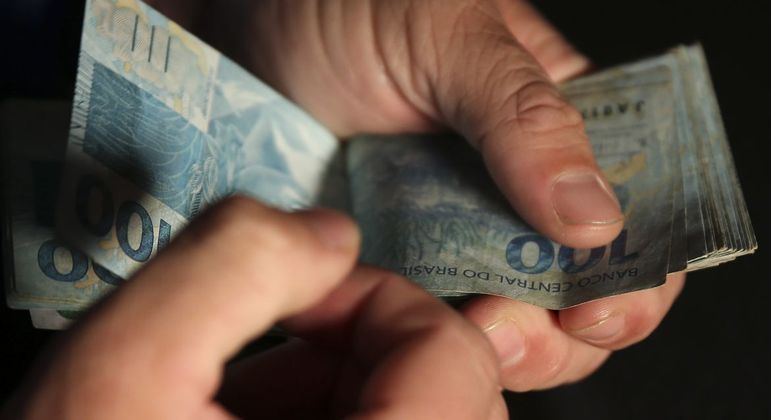 Mão masculina conta dinheiro de maço com notas de cem reais
