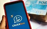 Mão segura celular com o aplicativo Caixa Tem, rodeado por cédulas de reais. Agência Estado / Adriana Toffetti / A7 Press