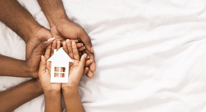 Mãos de criança e adultos com uma réplica de uma casa