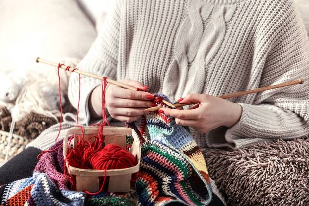 Mãos de mulher fazendo, em tricô, uma peça de roupa colorida. Freepik/pvproductions  