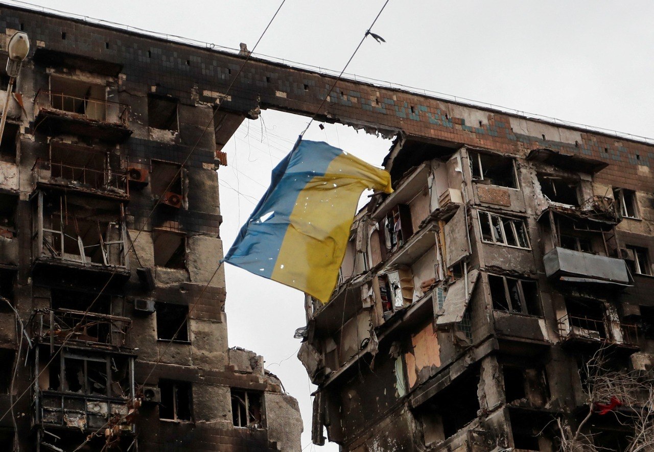 Bandeira da Ucrânia é vista pendurada em frente a um prédio destruído na Ucrânia 