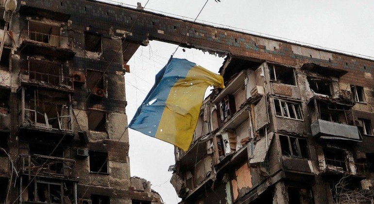 Bandeira da Ucrânia é vista pendurada em frente a um prédio destruído em Mariupol