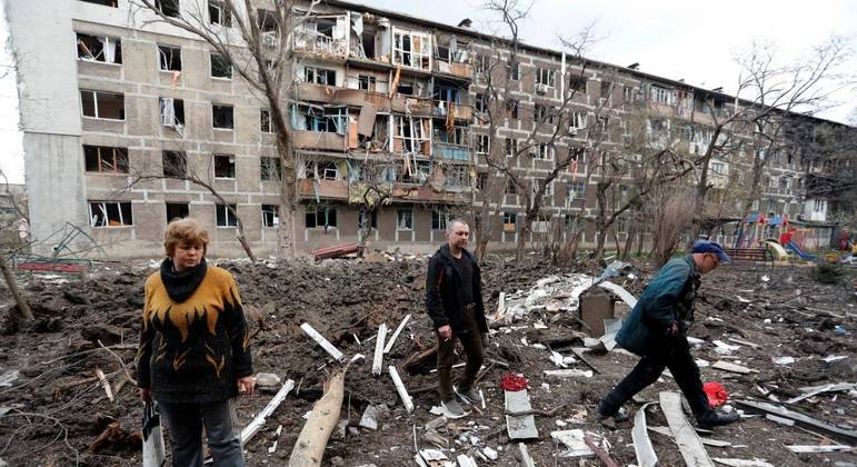 Moradores caminham perto de um bloco de apartamentos danificado em Mariupol