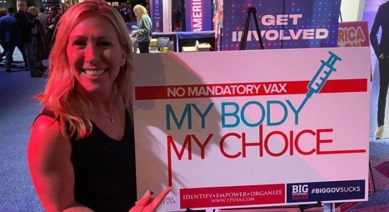 Marjorie segurando um cartaz que diz: "Não à vacina obrigatória; meu corpo, minha escolha"