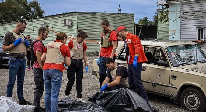 Membros da Cruz Vermelha observam corpos de civis encontrados na sexta (30)