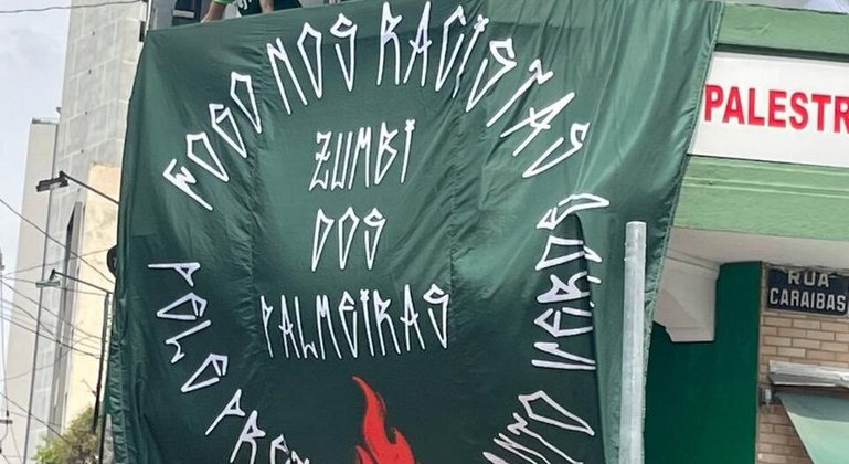 Bandeira está com a mensagem 'Fogo nos racistas. Pele preta, manto verde'. 